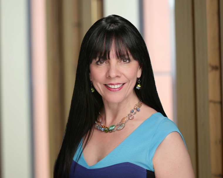 A portrait of Maria Manriquez wearing a blue top and smiling at the camera